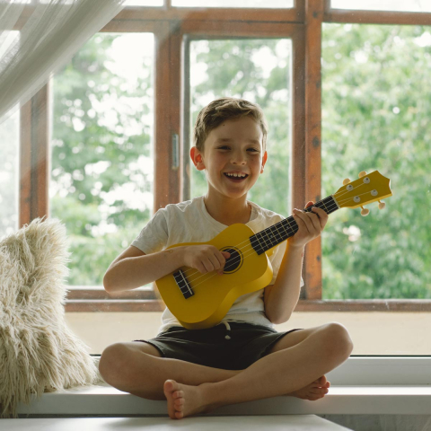 leiner Junge sitzt auf einer Fensterbank mit seiner gelben Gitarre