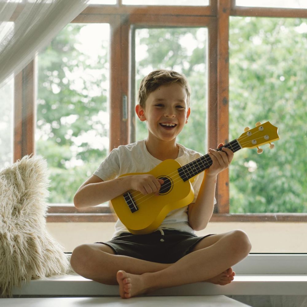 leiner Junge sitzt auf einer Fensterbank mit seiner gelben Gitarre